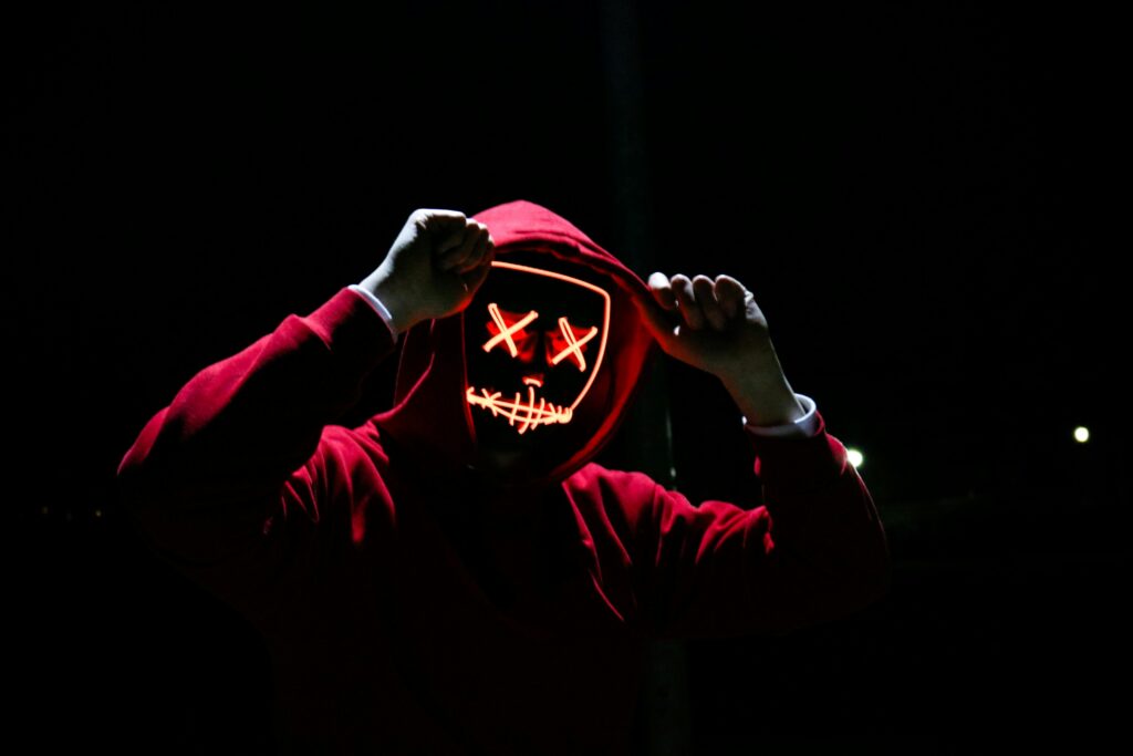 A spooky illuminated mask figure with a red hoodie in a dark setting, perfect for Halloween themes.